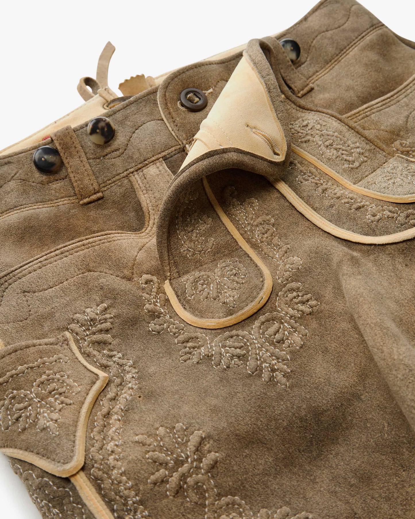Close-up of a brown leather jacket with floral embroidery on a white background