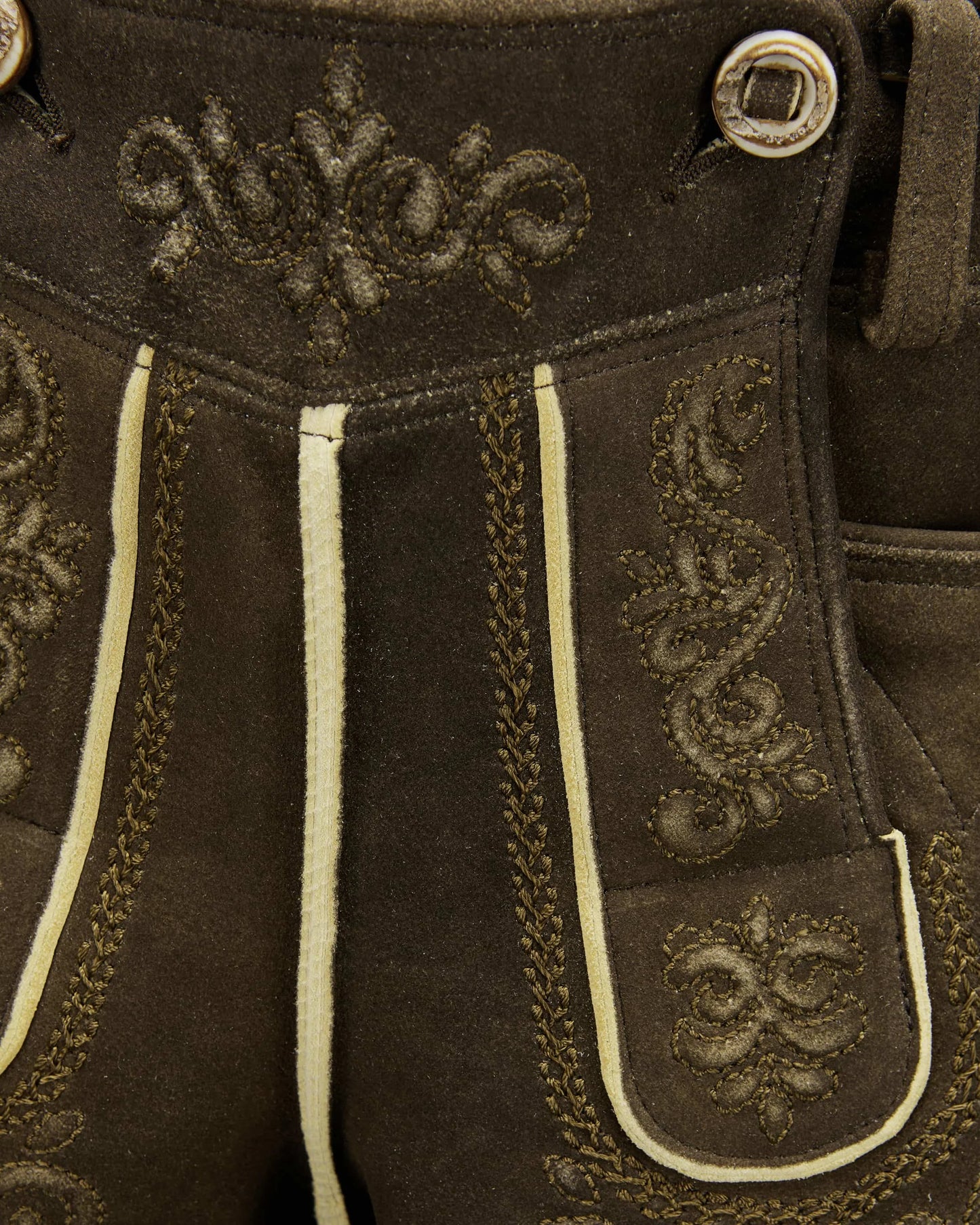 Close-up of brown leather pants with decorative stitching and buttons.