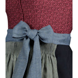 Close-up of a red patterned top with a blue bow and green pleated skirt on a white background