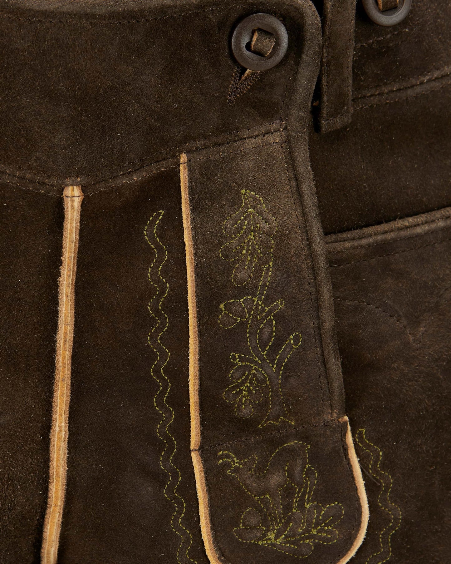 Close-up of brown suede fabric with embroidered designs and buttons.