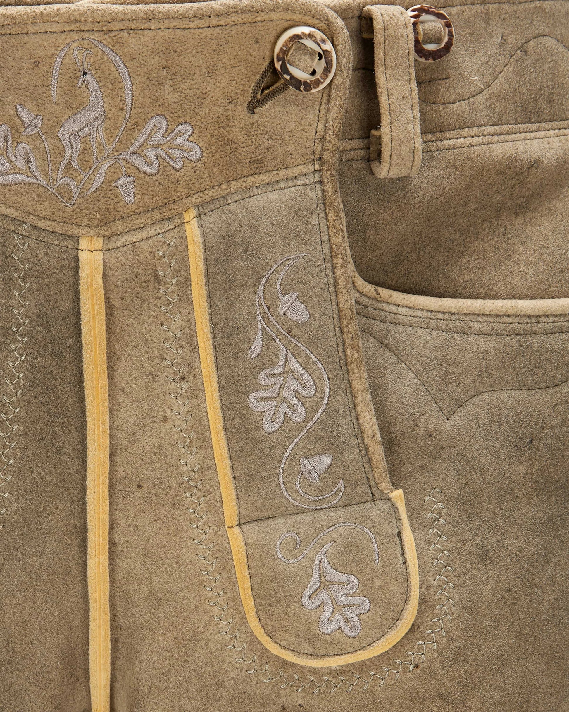 Close-up of brown leather pants with embroidery and button details