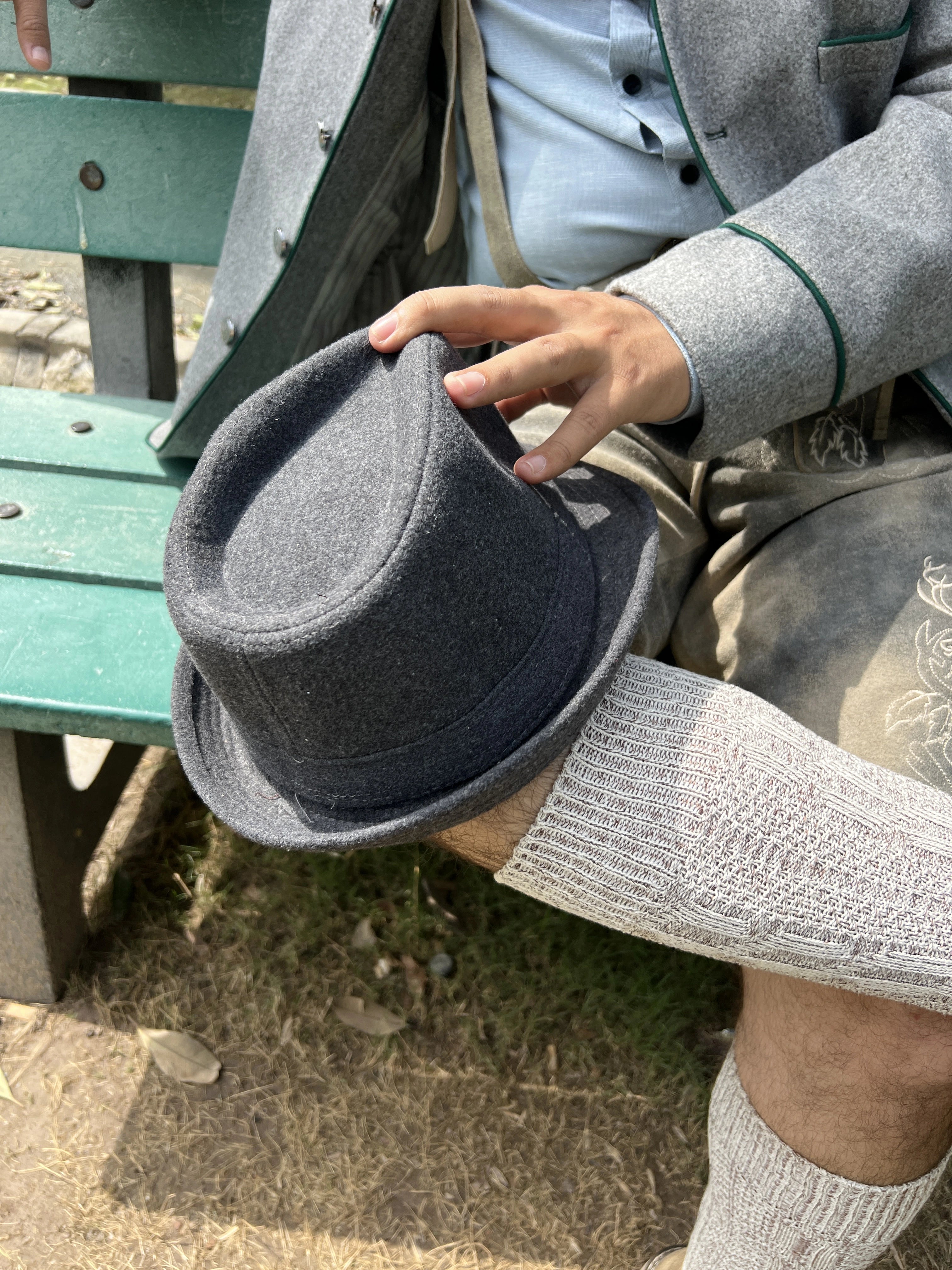 Person holding a gray fedora hat outdoors on a bench