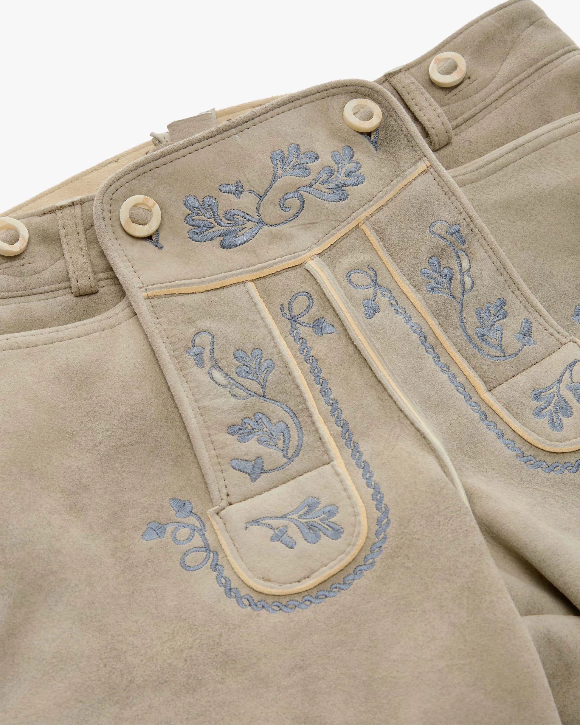 Beige pants with blue floral embroidery on a white background