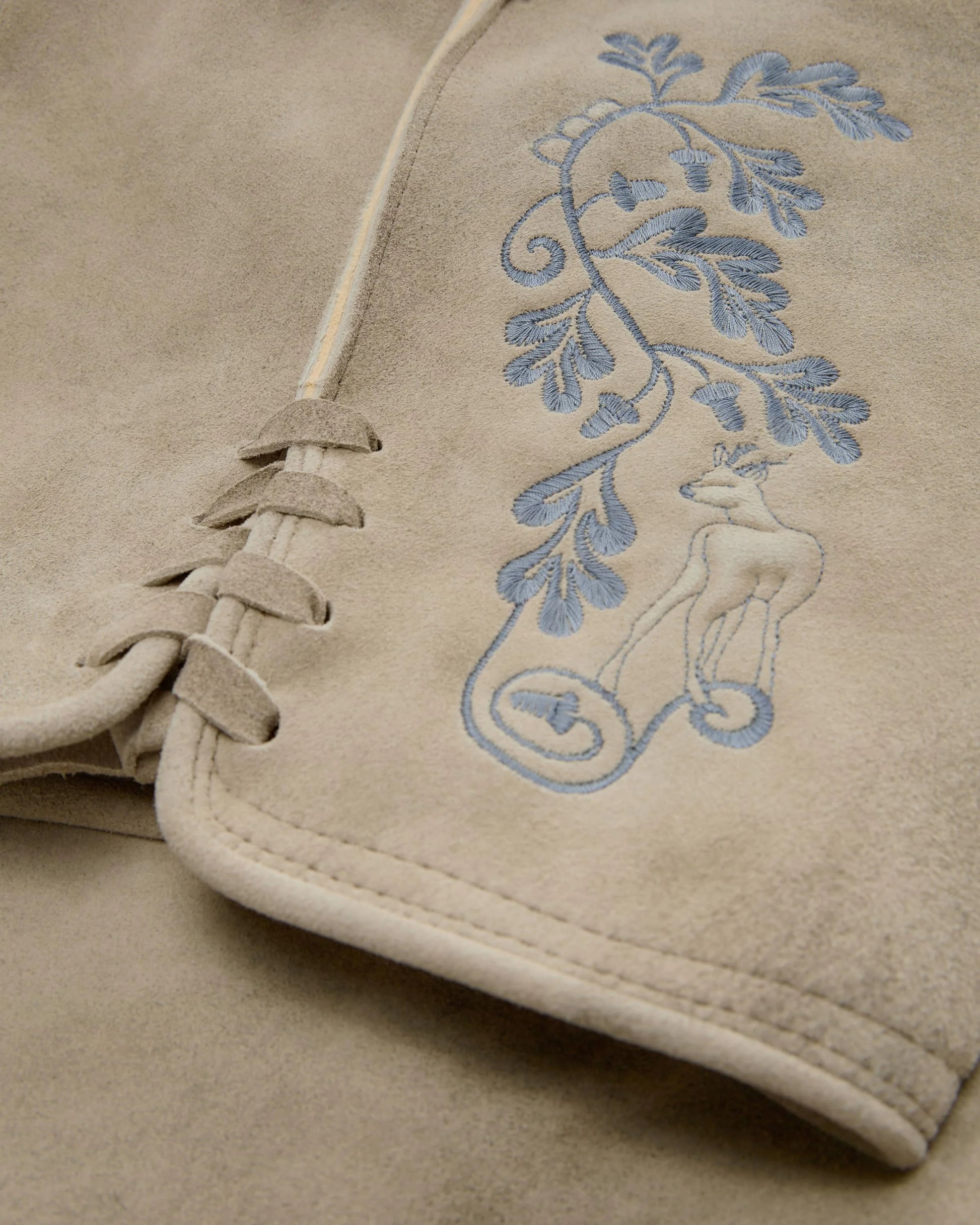 Close-up of beige fabric with blue embroidered design on a garment.