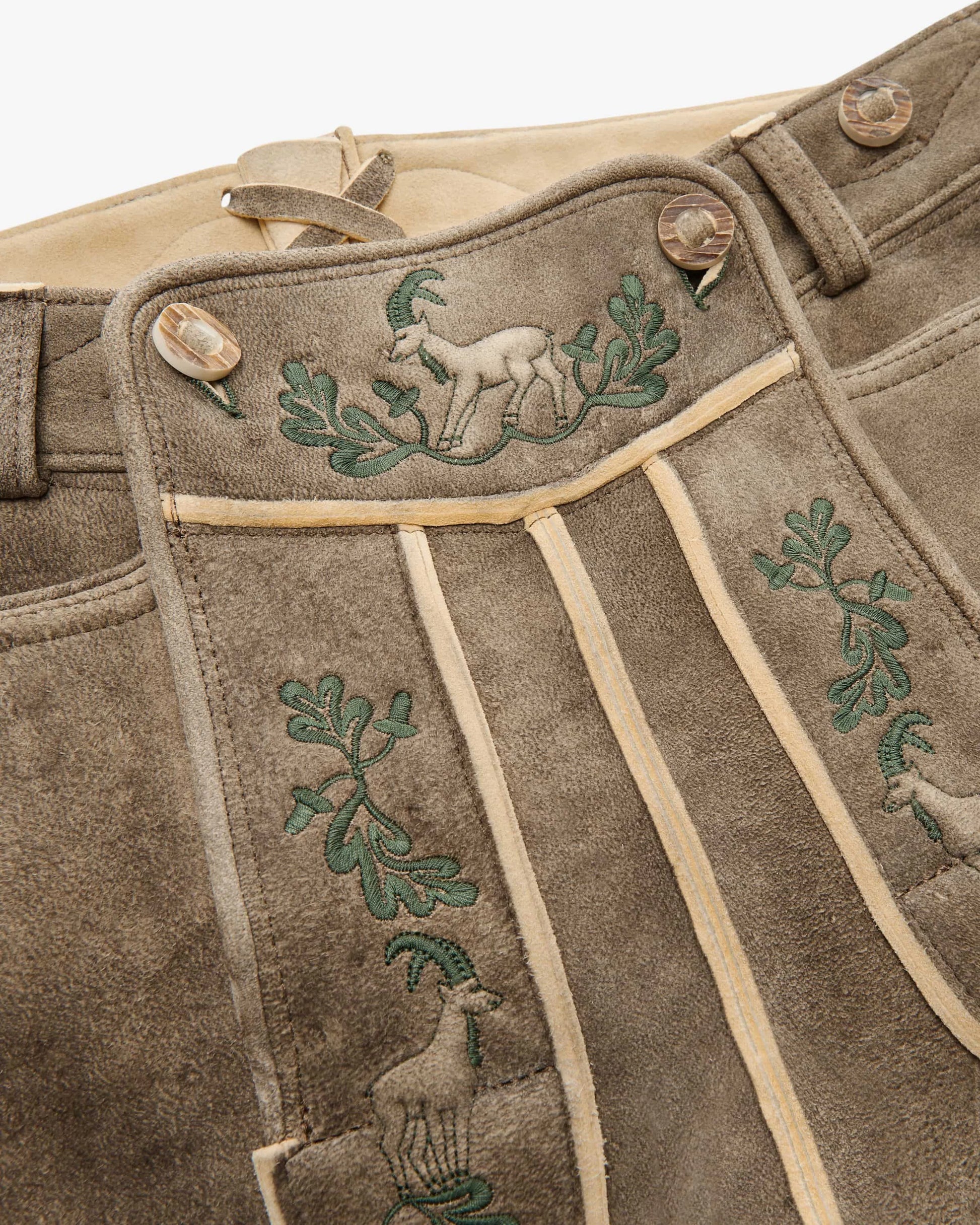 Brown leather pants with embroidered green designs of deer and leaves on a beige background