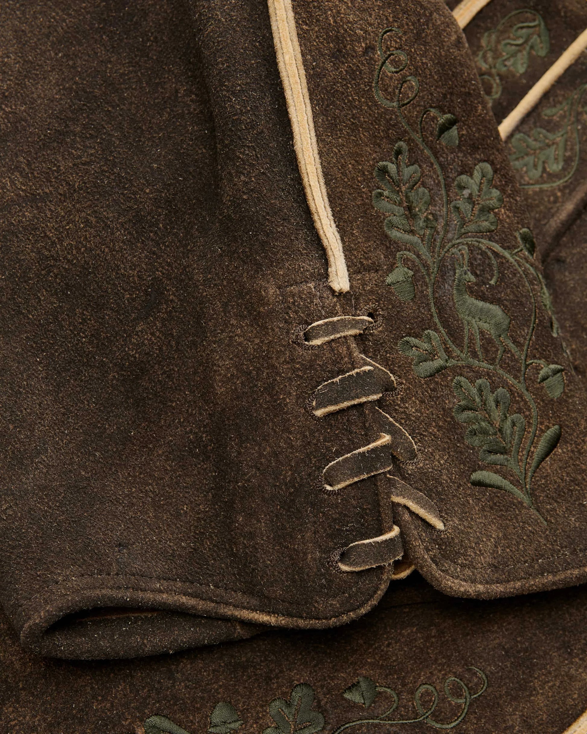 Close-up of a brown fabric with embroidered green leaves on a garment.