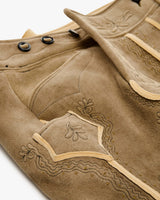 Close-up of a brown leather boot with intricate stitching and decorative elements on a white background