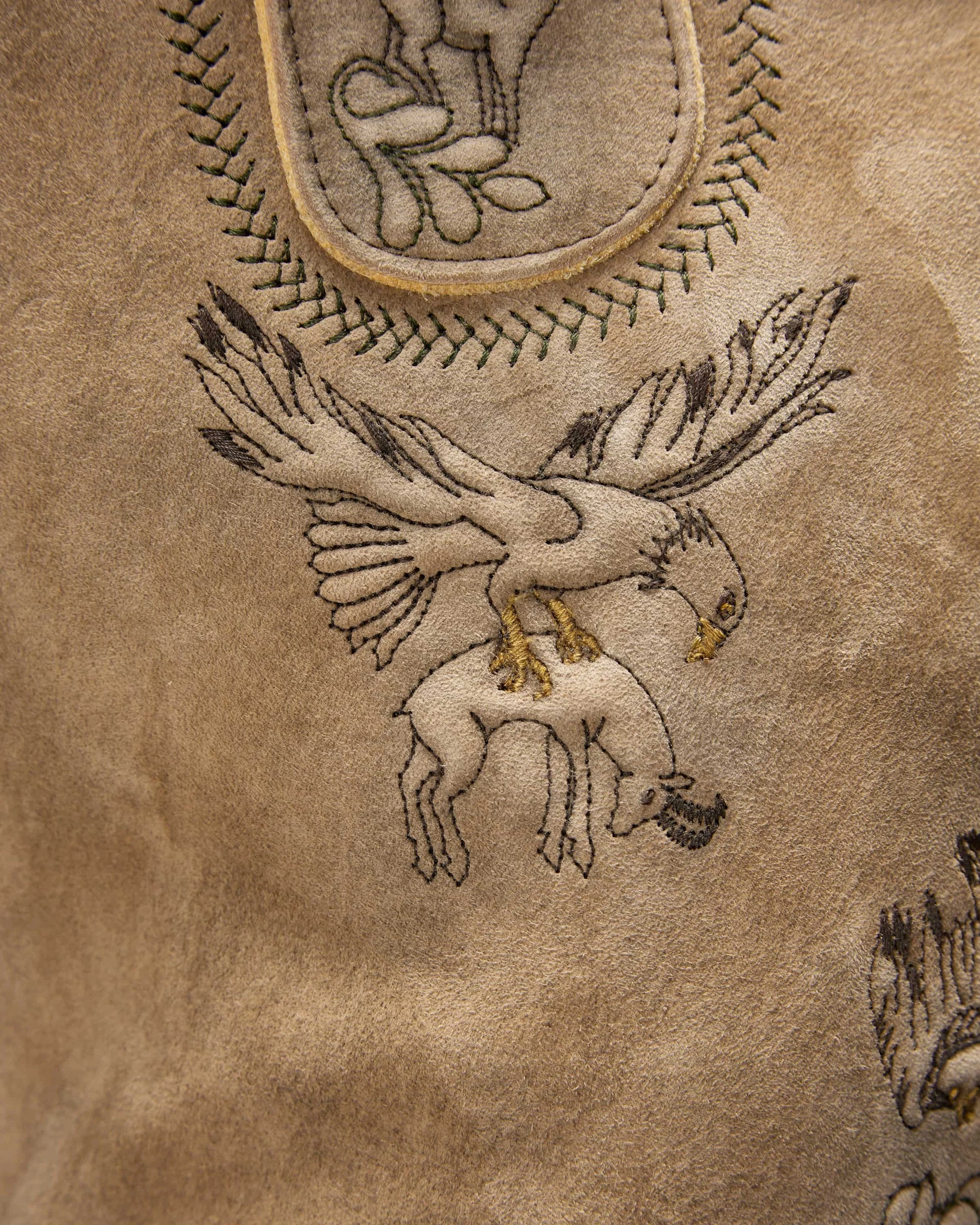 Embroidered design of a bird on a textured brown leather surface