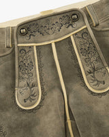 Close-up of brown leather pants with intricate floral embroidery on a beige background