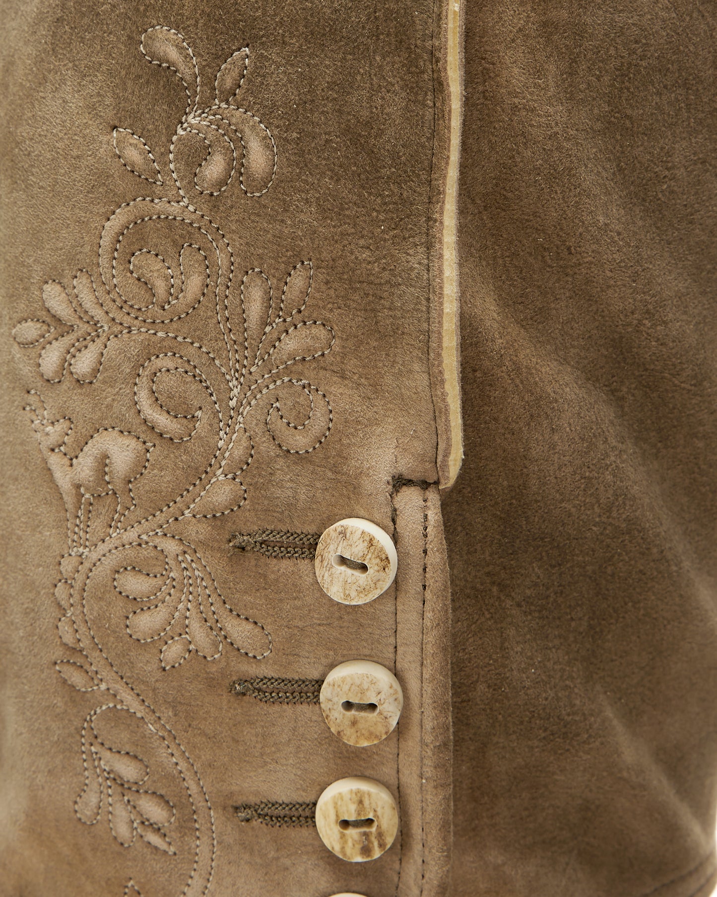 Close-up of a brown suede jacket with intricate embroidery and buttons.
