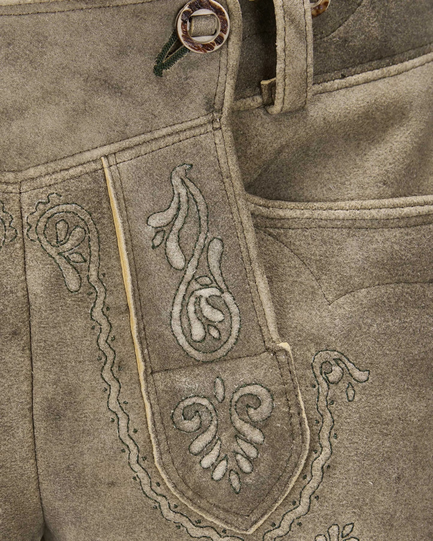 Close-up of a brown leather apron with intricate white embroidery on a matching background.