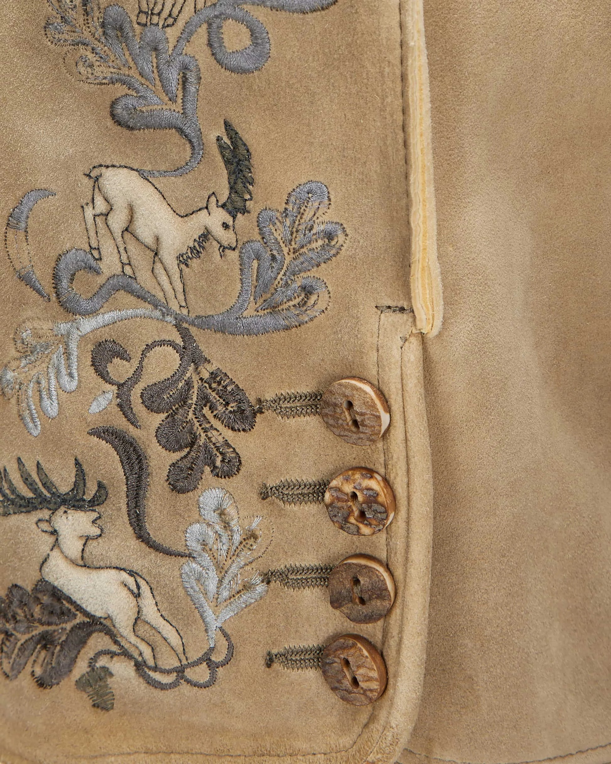 Close-up of a beige fabric with embroidered deer and floral patterns.